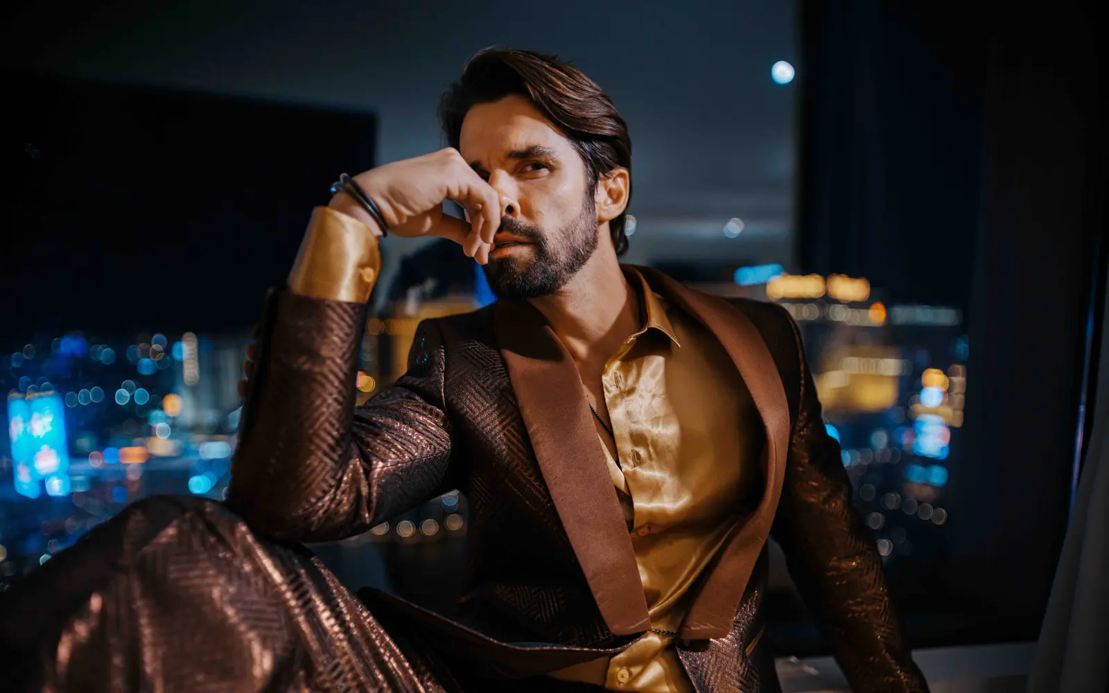 A man in a bronze suit and gold shirt sitting in front of a night window, city lights out of focus behind him — the sample photo the Lab effects run on.